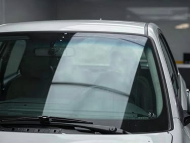 Freshly installed windshield on a vehicle inside a clean shop, glass catching bright overhead light, reflection crisp, Buenos Aires sky visible through the glass