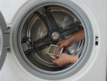 Wide environmental shot of a washing machine drum open in a laundry room, a technician's hands removing a clogged filter, shop lighting mixed with daylight, water-stained drum interior visible, real home setting