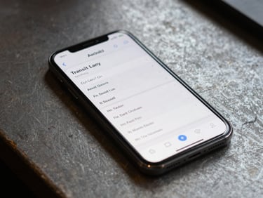 Android phone screen showing a transit scheduling app with high-contrast text, resting on a worn workbench surface, diffuse natural light from above, no hands visible
