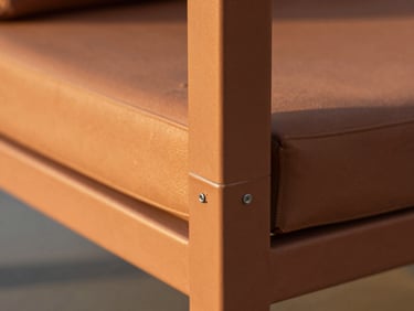 Macro detail shot of a flawless welded joint on a terracotta-colored aluminum outdoor sofa frame, warm golden hour light highlighting the subtle texture of the electrostatic paint, shallow depth of field.