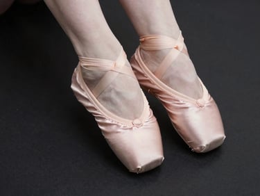 Close-up of elegant pink satin pointe shoes resting on a dark minimalist surface, soft side-lighting highlighting the clean stitching