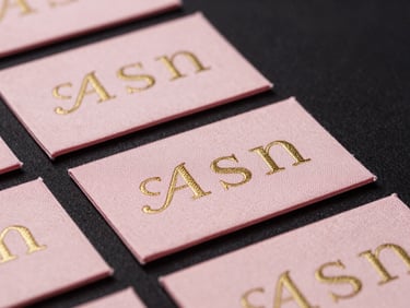 Macro shot of custom woven brand labels stitched into high-quality pink fabric, elegant gold lettering, sharp focus