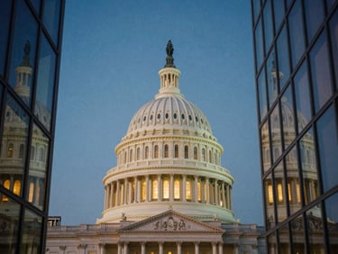 The neoclassical architecture of the U.S. Capitol dome framed through modern clean glass lines at dusk, deep blue sky, soft warm interior lights, editorial film.