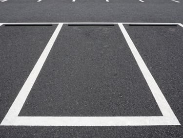 Straight-on eye-level shot of a clean, well-lit urban monthly parking lot in Tokyo, clear white line markings on dark asphalt, bright daylight with high visibility.