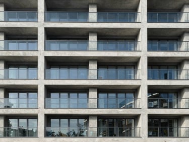 Straight-on architectural shot of a modern multi-family residential building exterior, sharp concrete lines, clean glass balconies under bright diffused morning light.