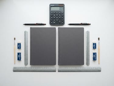 Symmetrical flat-lay of financial ledgers, a sleek modern calculator, and technical drafting tools on a clean white desk, bright overcast daylight, sharp focus