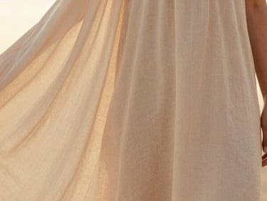 Editorial close-up of a woman in a flowing beige linen dress, soft golden-hour light, focusing on the elegant drape of the fabric