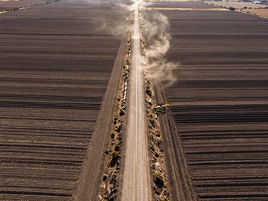 Wide-angle drone shot of perfectly graded agricultural roads cutting through rustic Mexican land, high-contrast sunlight, dust-lit environment