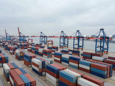 Aerial view of a container logistics port facility, rows of standardized shipping containers stacked in precise grid formation, cargo cranes visible, overcast industrial light