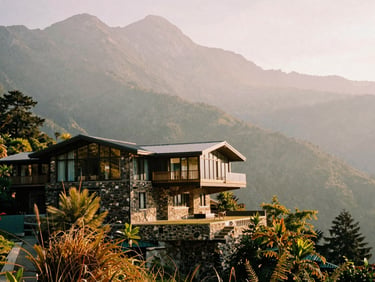 Wide-angle environmental shot of a cantilevered stone and glass villa on a mist-shrouded Himalayan peak during golden hour, 35mm film