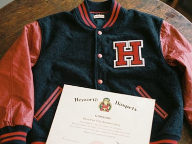 A close-up of a vintage Heyworth Hornets letterman jacket and high school diploma resting on a dark wooden table, warm nostalgic lighting, 35mm film style.