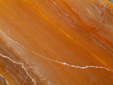 Overhead macro of polished Onyx Orange slab surface — translucent amber-orange tones with white vein lines, studio strobe lighting, tight orthographic framing
