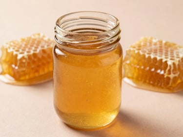 An amber glass jar of raw honey under golden natural light, honeycomb visible in the background, warm honey-gold tones, 35mm photography