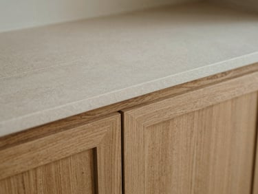 Tight macro shot of a raw travertine slab meeting brushed oak cabinetry, diffused morning daylight, highlighting tactile wood grain and stone texture.