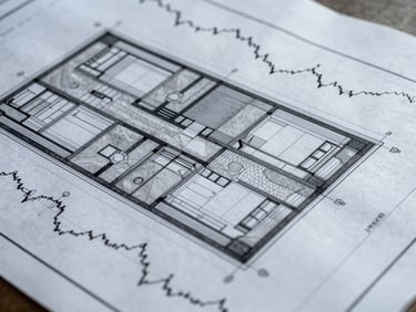 Close-up of a detailed architectural blueprint with overlayed financial graphs, cool overcast daylight, desaturated slate and concrete tones, sharp focus, 35mm lens
