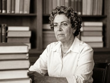 Archival sepia-toned portrait of a contemplative Brazilian academic, Prof. Ana Lúcia Costa, surrounded by research documents, soft natural library light, matte texture, historical archival feel, 35mm.