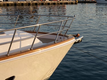 Yacht stern at rest in calm harbor water, La Paz, golden hour light on polished teak rail and stainless hardware, crew hand adjusting a dock line, no passengers