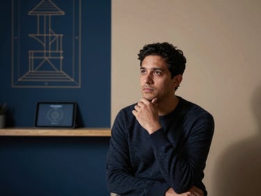 Professional portrait of a male astrologer in thoughtful pose, warm interior lighting, soft shadows, 35mm, abstract architectural diagram on a tablet in the background