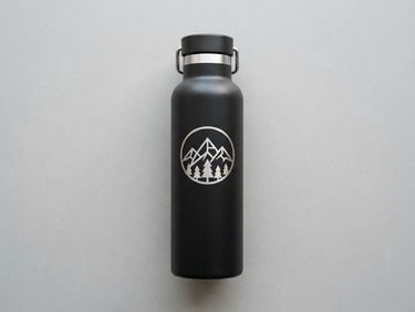 Minimalist flat lay of a matte black thermal water bottle with a laser-engraved emblem, soft shadows, neutral grey background.