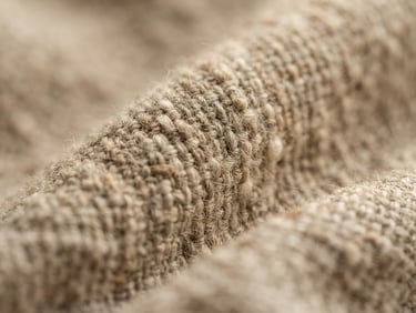 Extreme close-up of soft oatmeal linen weave, warm diffused morning light, shallow depth of field, tactile fabric textures