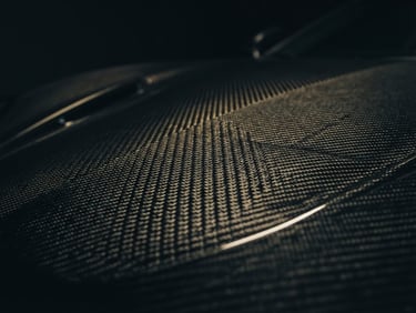 Extreme close-up of a carbon fiber weave on a supercar hood, dramatic low-key studio lighting, gold rim highlights, 35mm anamorphic