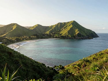Wide environmental shot of Lombok's pristine coastline at sunrise, deep green hills meeting clear water, warm natural daylight, clean editorial composition.