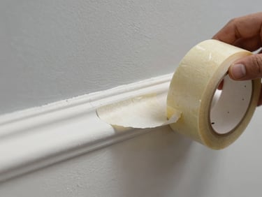 Macro close-up of a hand peeling crisp masking tape from a slate grey wall, revealing a laser-straight, flawless white trim line under bright, natural daylight.