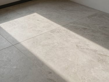 Overhead shot of large-format porcelain tile floor, tight grout lines, level surface under diffuse window light, grey-and-cream color tones