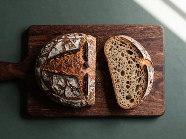 Overhead minimalist flat-lay of a rustic sourdough bread sliced on a dark wooden board, soft natural side light, rich crimson tones, 35mm