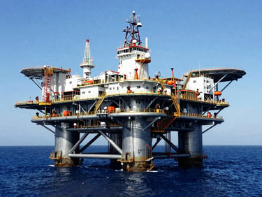 Wide environmental shot of an offshore oil platform in Rio de Janeiro during bright daylight, steel structures reflecting the sun, deep blue ocean, high-contrast industrial editorial photography, 35mm.