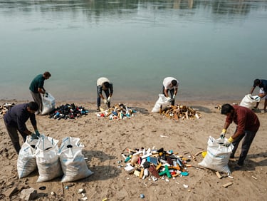 Overhead wide-angle documentary photograph of a Narmada river cleaning mission in progress, workers on a sandy bank sorting debris into labelled piles, natural daylight, river visible in the background, worn gloves and collection sacks in the foreground