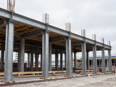 Active construction site in progress with structural columns, wide environmental shot, desaturated steel tones, 35mm