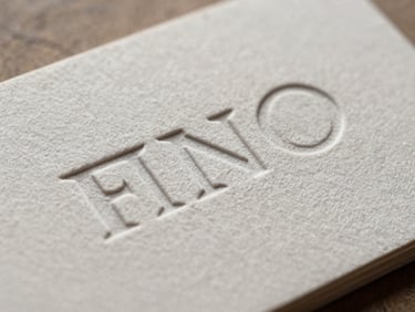 Close-up of a brand identity mark printed on thick cotton business card stock, debossed letterform visible, north daylight, sharp paper grain detail