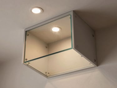 45-degree overhead angle of a glass and mirror storage unit built into a residential wall niche, clean matte hardware, warm ambient light from a recessed ceiling fixture revealing the depth of the cavity and material layering
