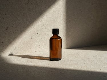 A minimalist amber glass bottle of bath oil resting on raw travertine stone, sharp shadows, low-angle direct sunlight.