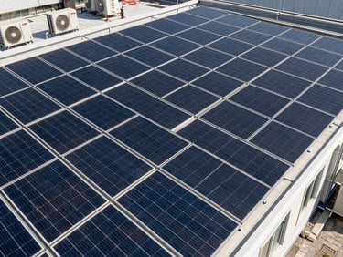 Overhead 45-degree angle of a commercial flat rooftop covered in a dense grid of solar panels, hard midday shadows defining each module row, rooftop HVAC units visible at the far edge, no people