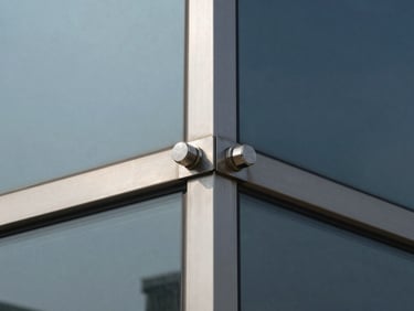 Crisp architectural photography of a four-way brushed steel spider fitting holding large glass panels, cool daylight, sharp shadows.