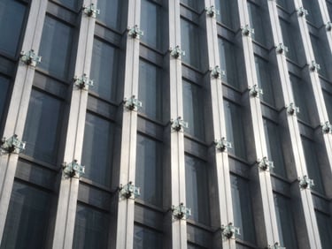 Low-angle architectural shot of heavy-duty glass spider connectors and stainless steel columns on a high-rise building facade, cool daylight, sharp shadows
