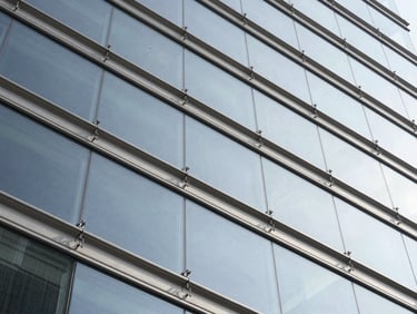 Low angle architectural shot of a glass facade suspended by stainless steel spider connectors, crisp daylight, 50mm lens