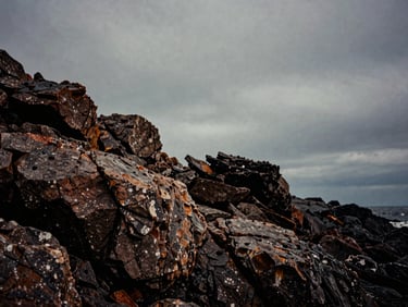 Extreme wide location scouting shot of a dramatic rocky coastline under heavy overcast skies, low-key lighting, rich analog grain, 35mm format