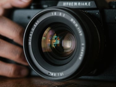 Close-up of a physical 35mm camera lens, reflection of set lights in the glass, hands adjusting focus, low-key dramatic lighting