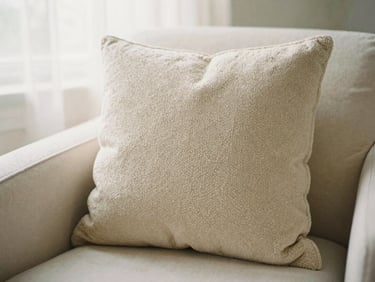 Textured bouclé cushion on a light armchair, close-up, soft focus, warm light, 35mm