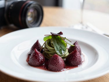 Close-up of a camera lens focusing on a beautifully plated dish in a Scandinavian-style restaurant, soft natural window light, rich crimson and forest green tones, shallow depth of field