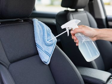 Clean car interior with professional detailer sanitizing dark fabric seats, bright focus