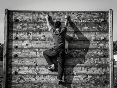 Cadet climbing a high wooden obstacle wall, outdoor tactical training ground, high contrast desaturated tones