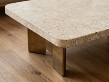 A low sculptural coffee table combining a textured travertine top with brushed bronze legs, empty negative space, 35mm