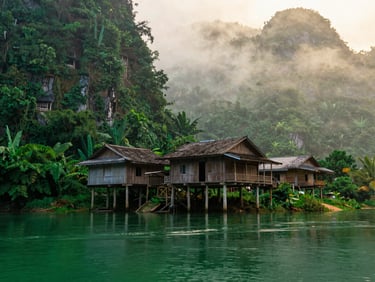 Traditional wooden stilt house of Tay people by the emerald Quay Son river, misty morning, atmospheric lighting