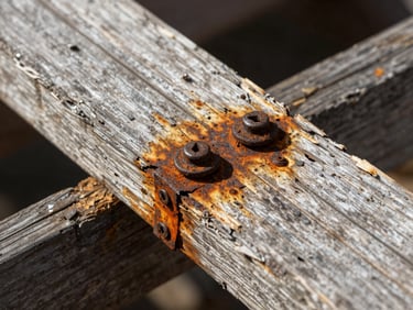 Macro shot of a rotted deck ledger board, rusted fasteners, and water-damaged house framing, harsh natural light showing decay.