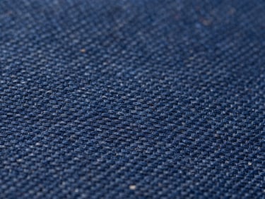 Macro close-up of deep indigo woven fabric showing the precise interlacing of warp and weft threads under bright daylight.