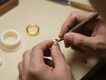 Hands of a master jeweler detailing a wax mold for a custom gold ring, warm workbench lighting